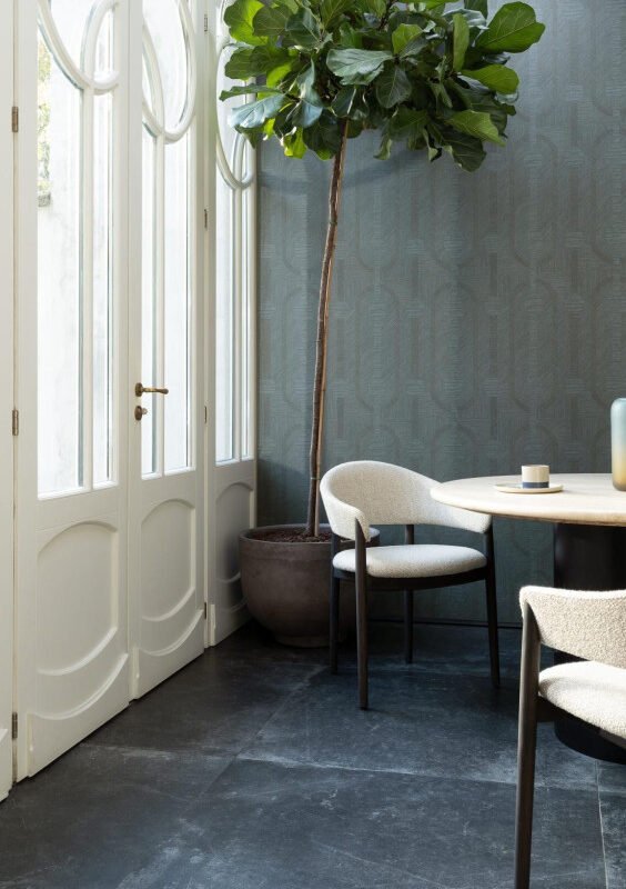 Salle à manger lumineuse avec papier peint géométrique vert canard Essentials Luxor Amulet 19413, chaises bouclées blanches et plante d'intérieur.