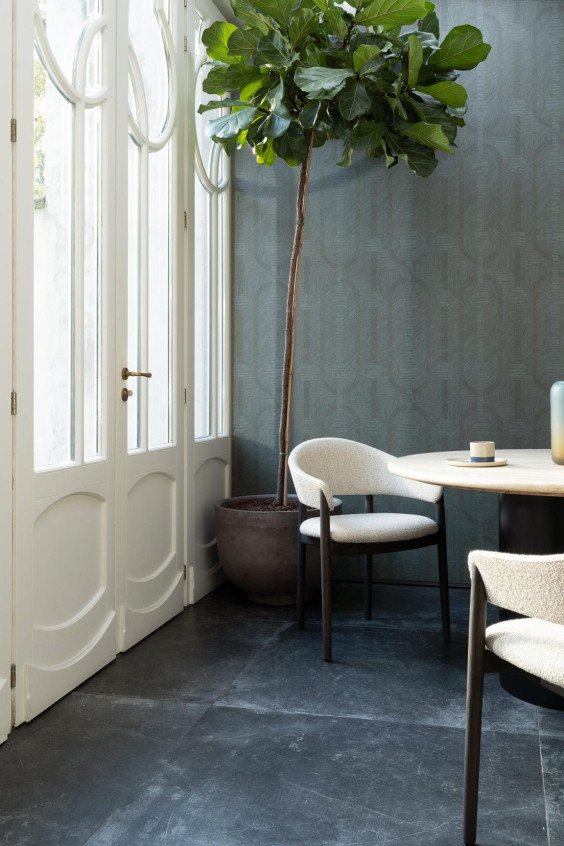 Salle à manger lumineuse avec papier peint géométrique vert canard Essentials Luxor Amulet 19413, chaises bouclées blanches et plante d'intérieur.