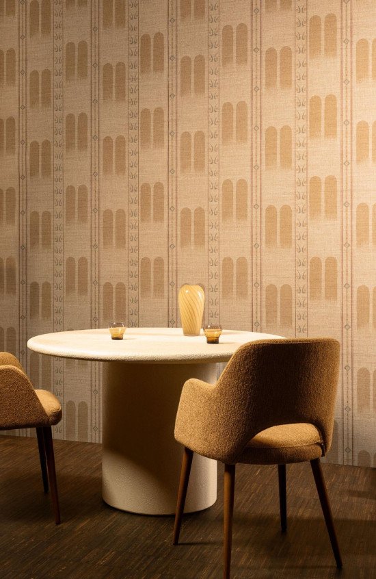Salle à manger moderne décorée du papier peint Indienne Poona 18300 à motifs d'arches sable et ocre avec table ronde en pierre.
