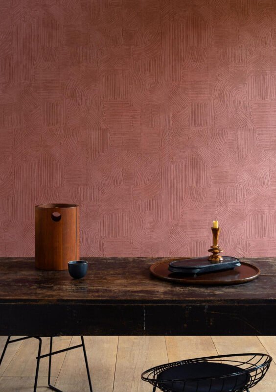 Table en bois massif foncé et objets d'art devant le papier peint terracotta à relief gravé Tali Tamba 60728.