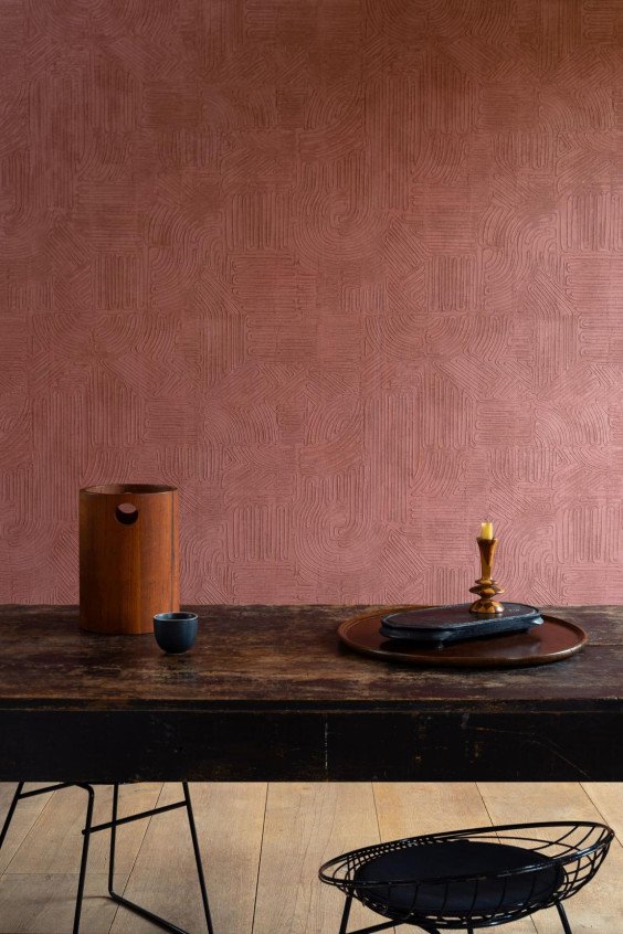 Table en bois massif foncé et objets d'art devant le papier peint terracotta à relief gravé Tali Tamba 60728.