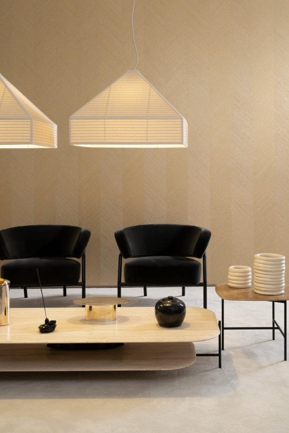 Salon moderne avec papier peint beige motif chevron Zephyr Kinisi 48602, fauteuils noirs et suspensions lumineuses en papier.