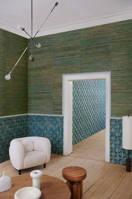 Papier peint texturé AllNaturals Sambe vert et bleu dans un salon moderne avec fauteuil bouclette blanc.