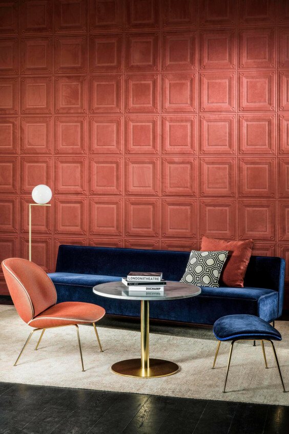 Papier peint effet caissons terracotta Spectra Caisson dans un salon moderne avec canapé bleu nuit et fauteuil orange.